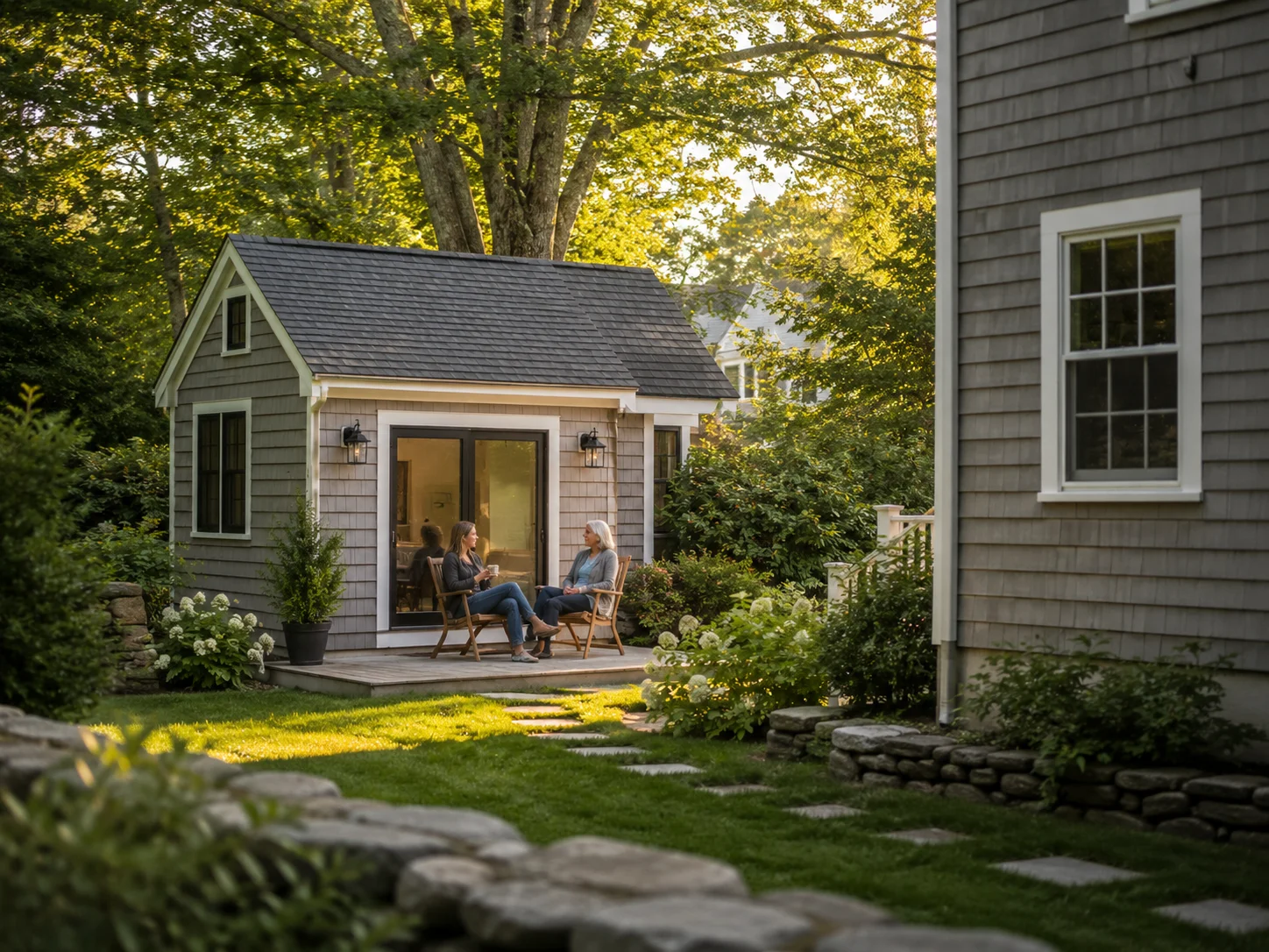 Two people sitting outside a detached accessory dwelling unit in a New England backyard.